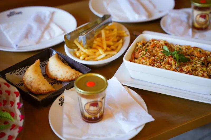 Mesa com pastéis, fritas, arroz de camarão e pudim no copo
